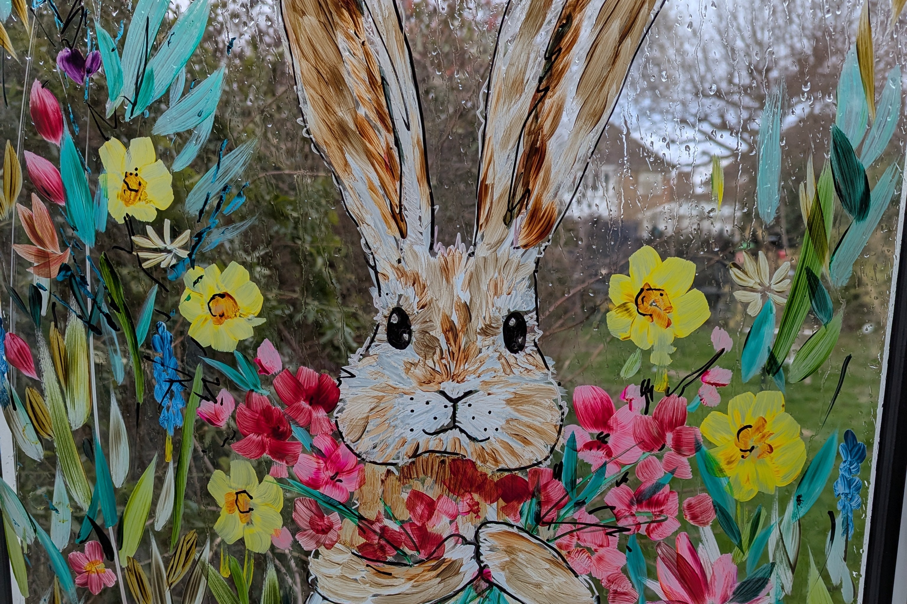 A colorful Easter themed window painting featuring a rabbit surrounded by flowers and Easter eggs.
